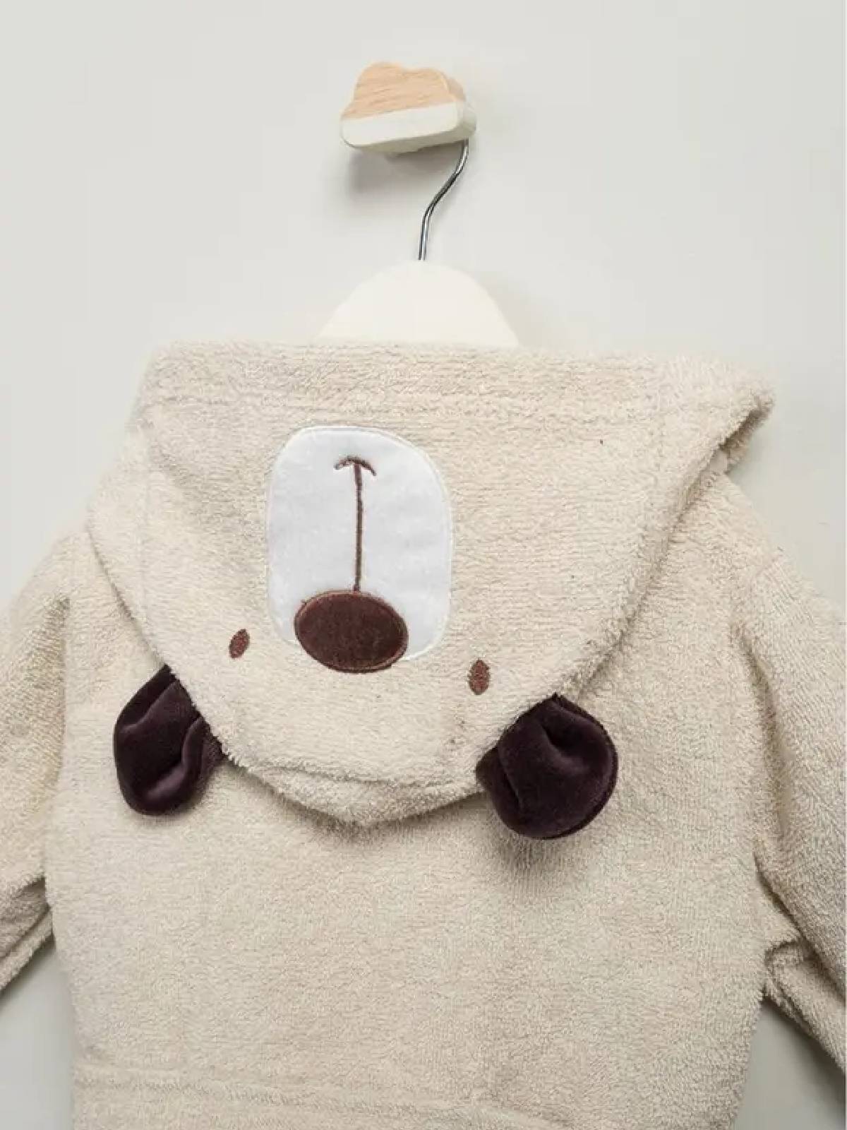 Ayıcık kapüşonlu, krem renkli bebek bornoz takımı; bornoz, panço havlu ve terlikten oluşan 3’lü set, beyaz fonda düz zemin üzerinde.